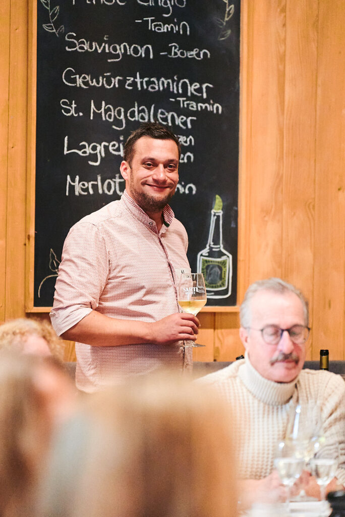 Service-Mitarbeiter mit Weinglas vor der beschrifteten Weintafel an der Floßlände in Augsburg