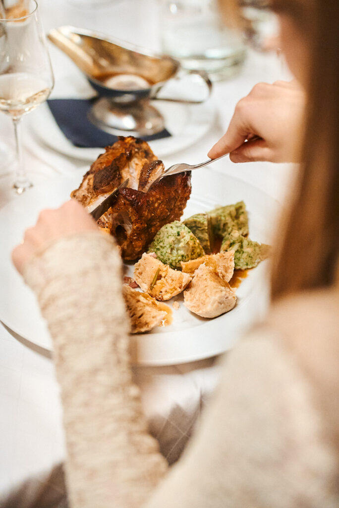 Ein Gast schneidet ein Stück von der Schweinshaxe auf seinem Teller – Törggelen an der Floßlände in Augsburg